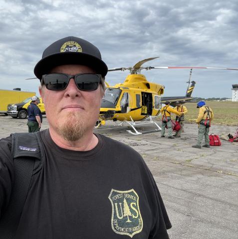 Daniel Patterson on duty for Forest Service firefighting crew with helicopter in background